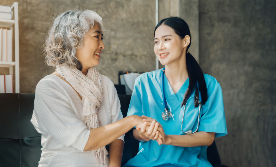 A friendly nurse in light blue scrubs holding hands with a smiling senior woman, showcasing compassionate hospice care.