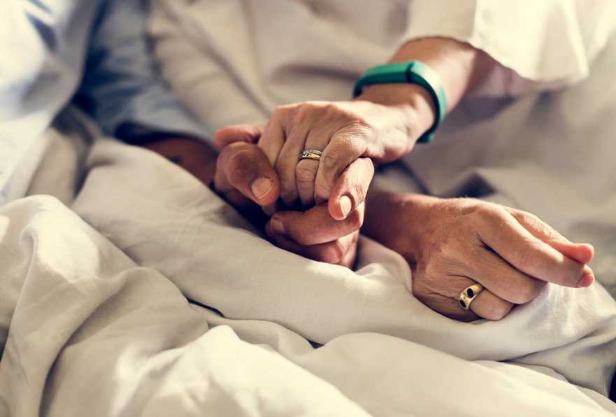 Family member holding the hand of a patient in bed, symbolizing compassionate end-of-life hospice care and comfort.